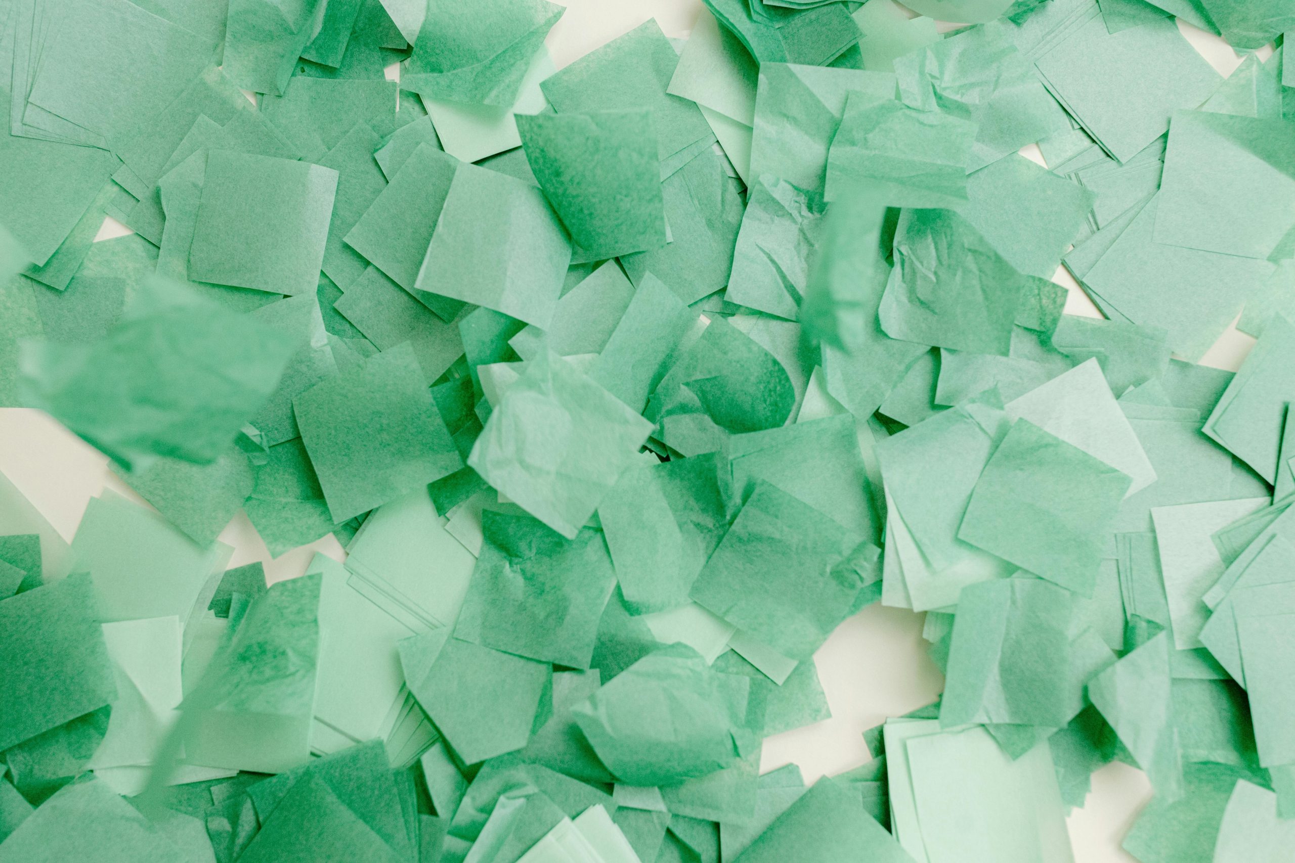 Abstract composition of overlapping green paper squares creating a vibrant textured pattern.