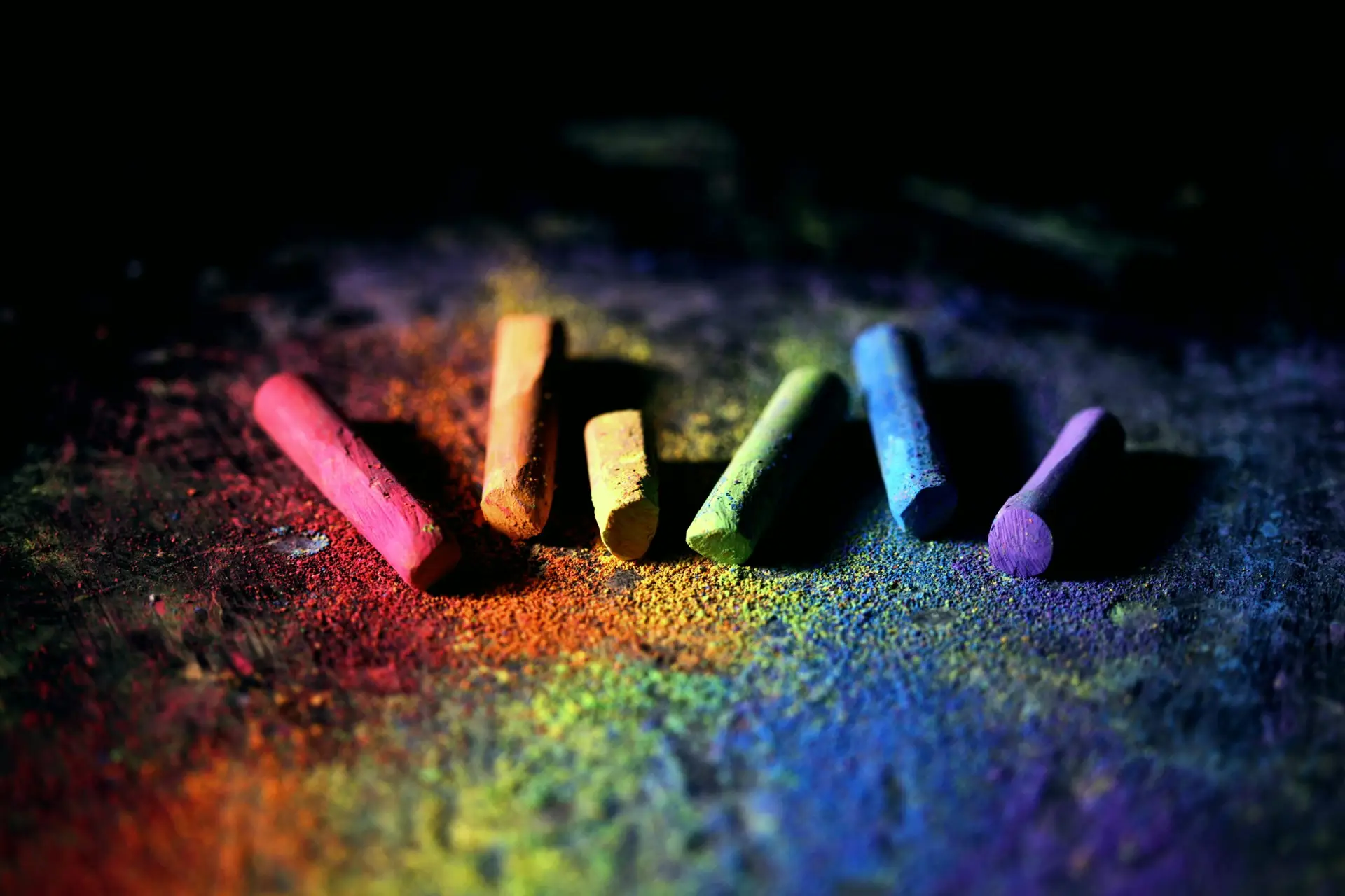 Colorful rainbow chalk pieces on dark background with chalk dust.