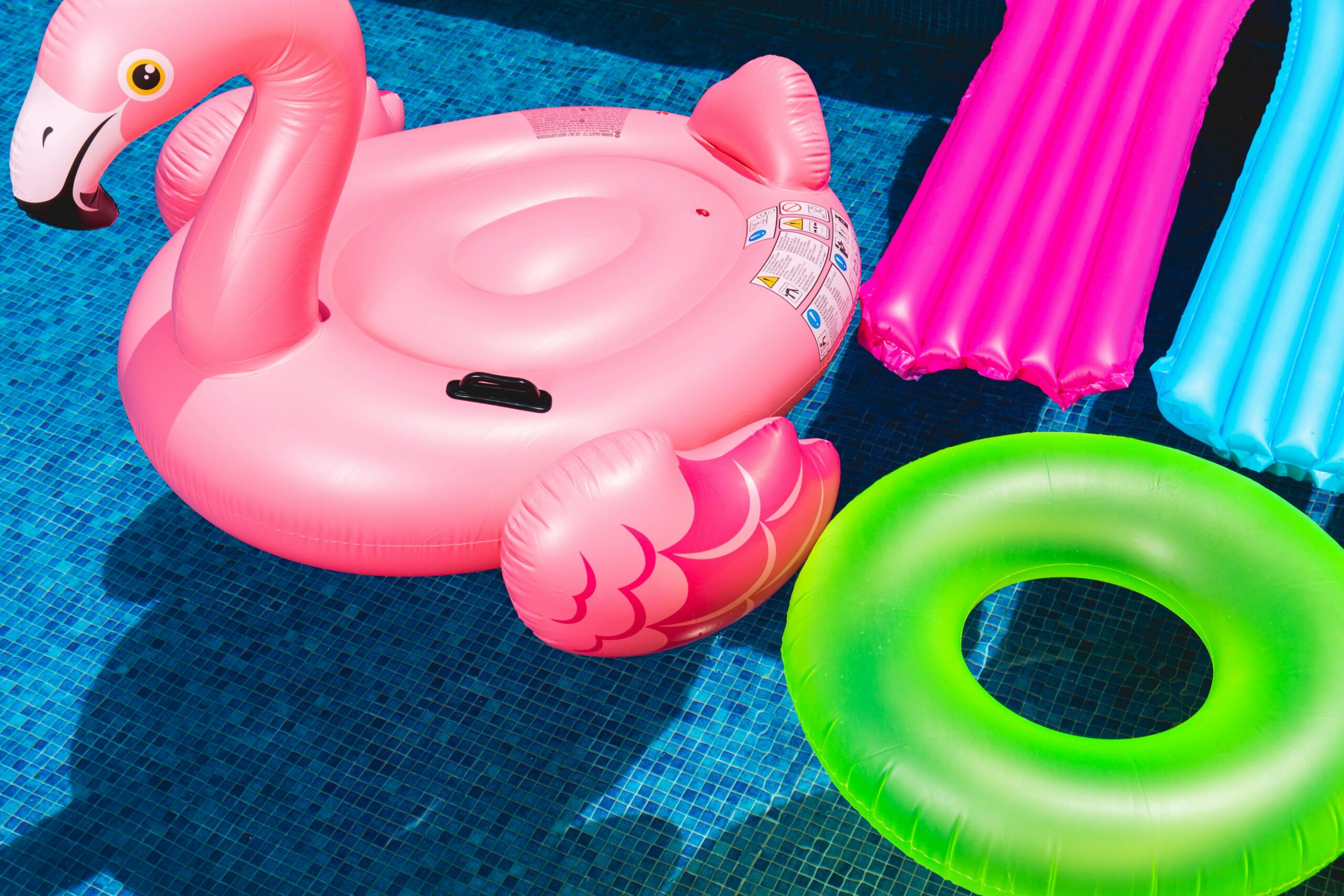 Bright inflatable flamingo and rings floating in a sunny pool.